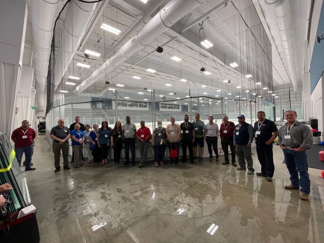 Group of people standing in an ice rink. Many wearing name tags, looking towards the camera.