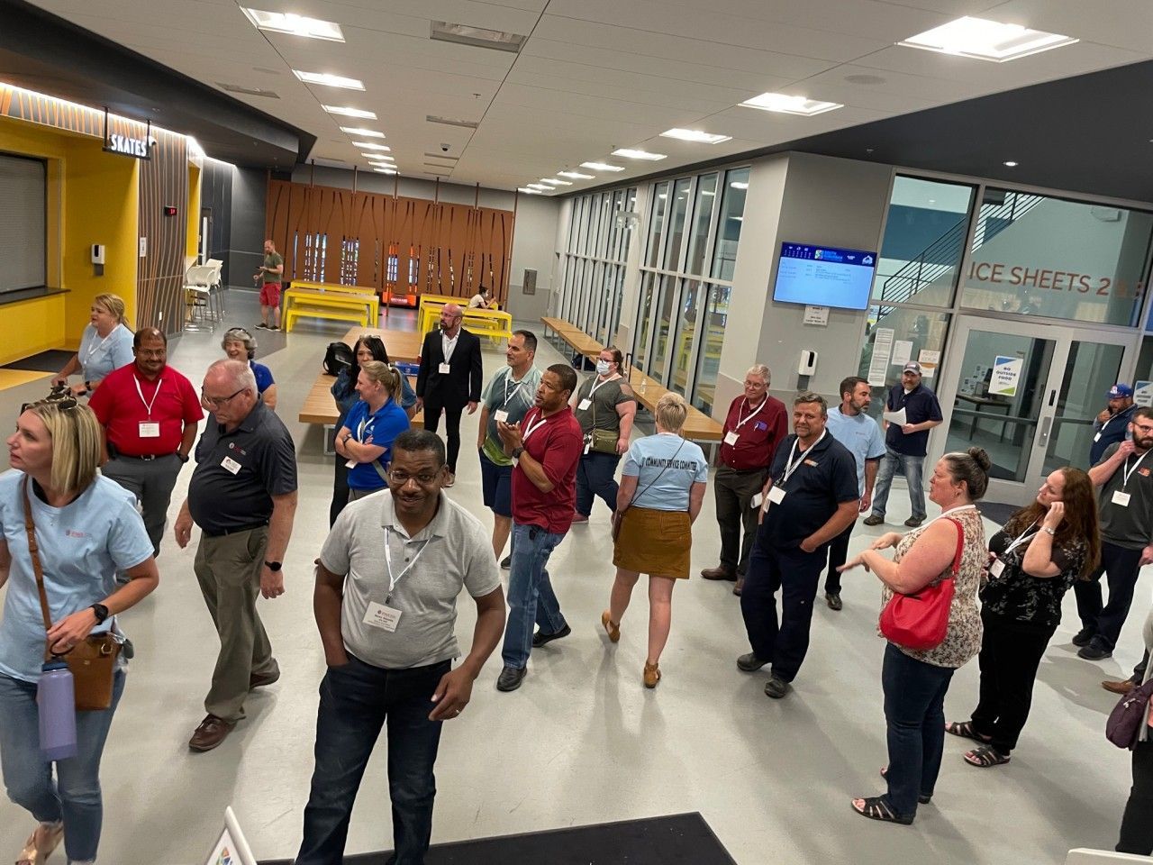 People in a lobby, some wearing name tags. Open doorway, walls are gray and yellow.