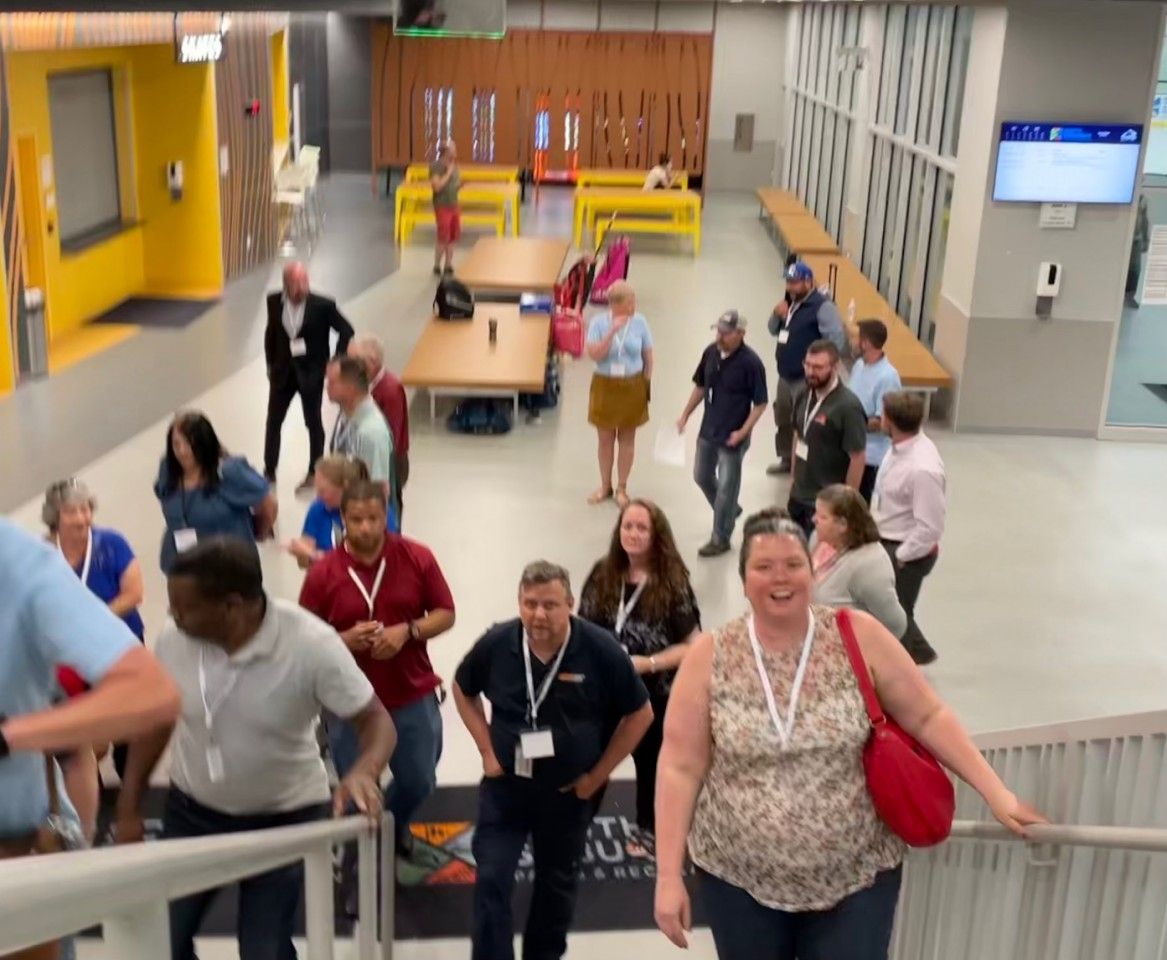 People walking up and down stairs in a modern building with yellow and gray walls. Some wear lanyards.