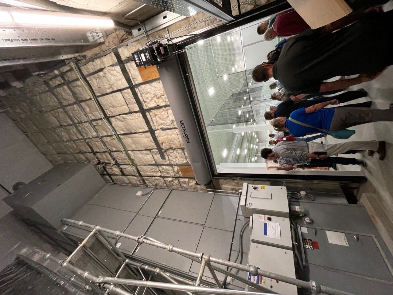 People standing near an open industrial door, looking into a large room with a high ceiling.