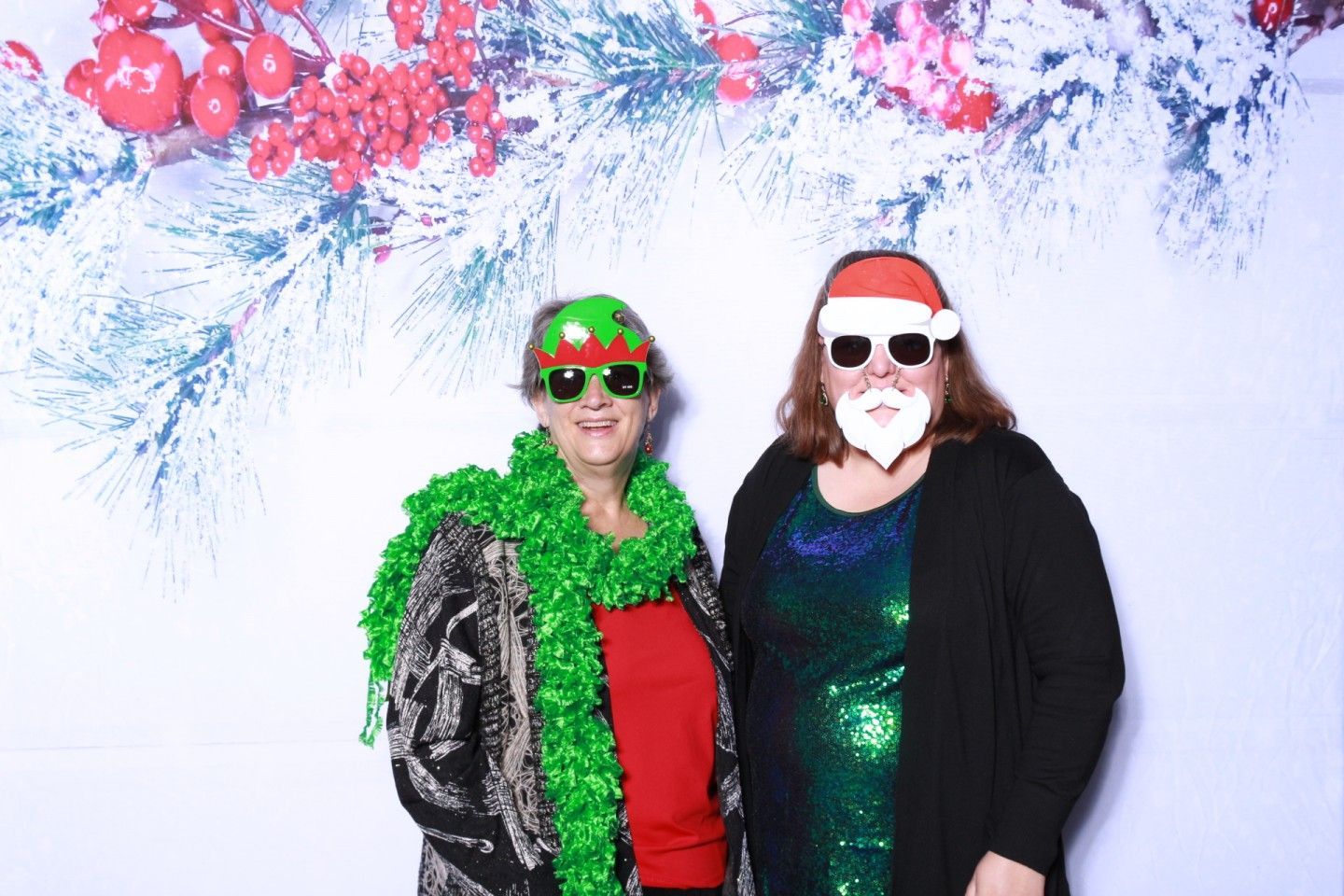 Two people in holiday attire posing in front of a festive backdrop.
