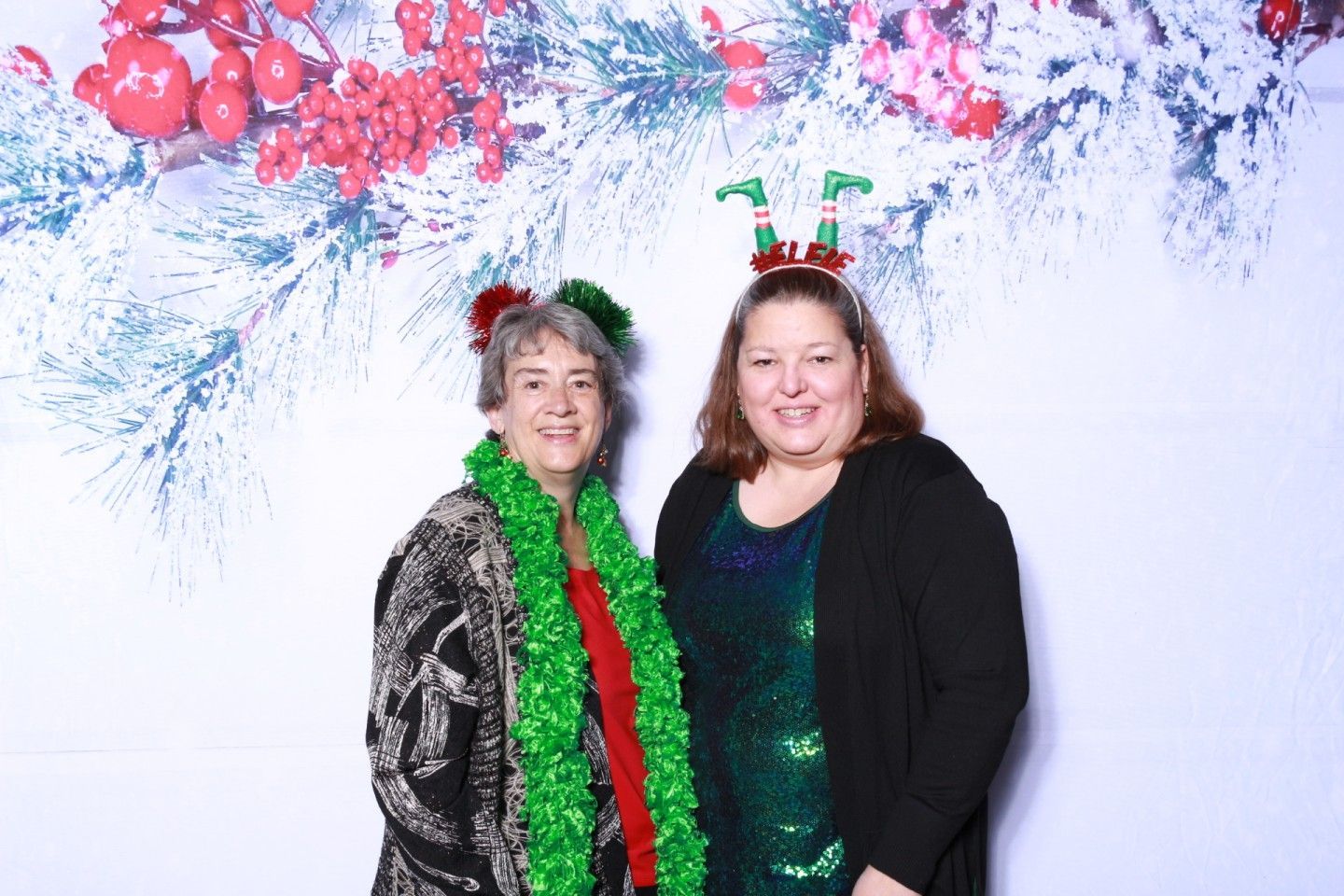Two people at a holiday party; one in a black and red patterned coat, other in a green sequin dress.