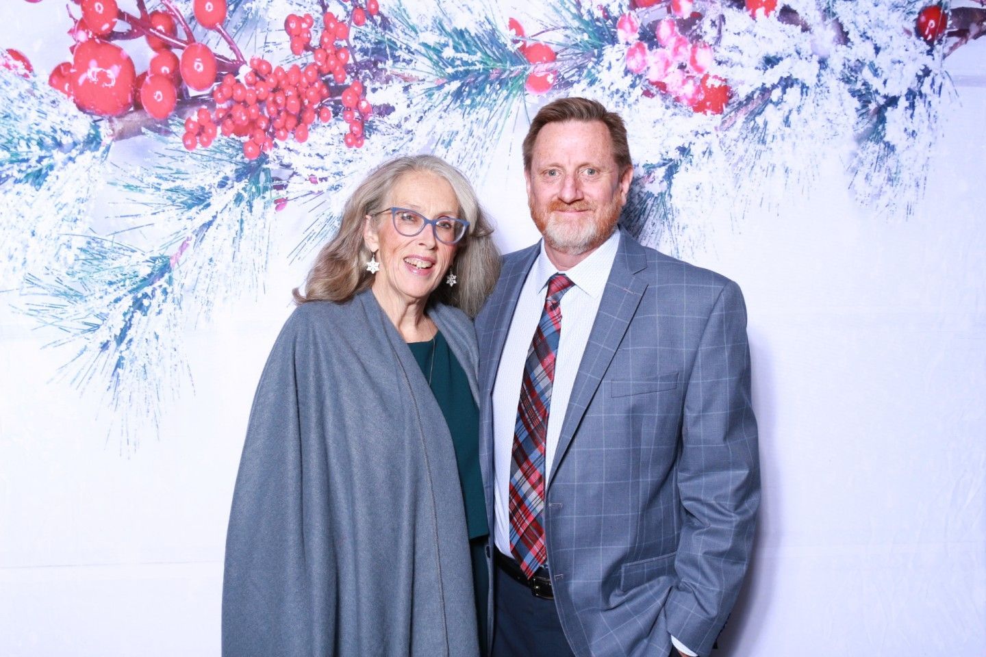 Couple posing in front of a festive backdrop with red berries and snowy branches.