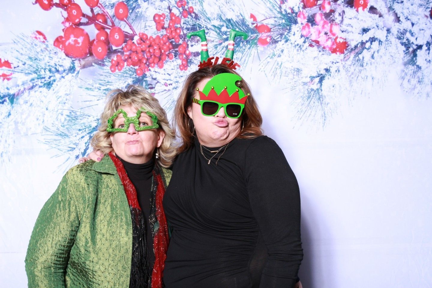 Two people pose in front of a holiday backdrop, wearing elf-themed glasses and headbands.