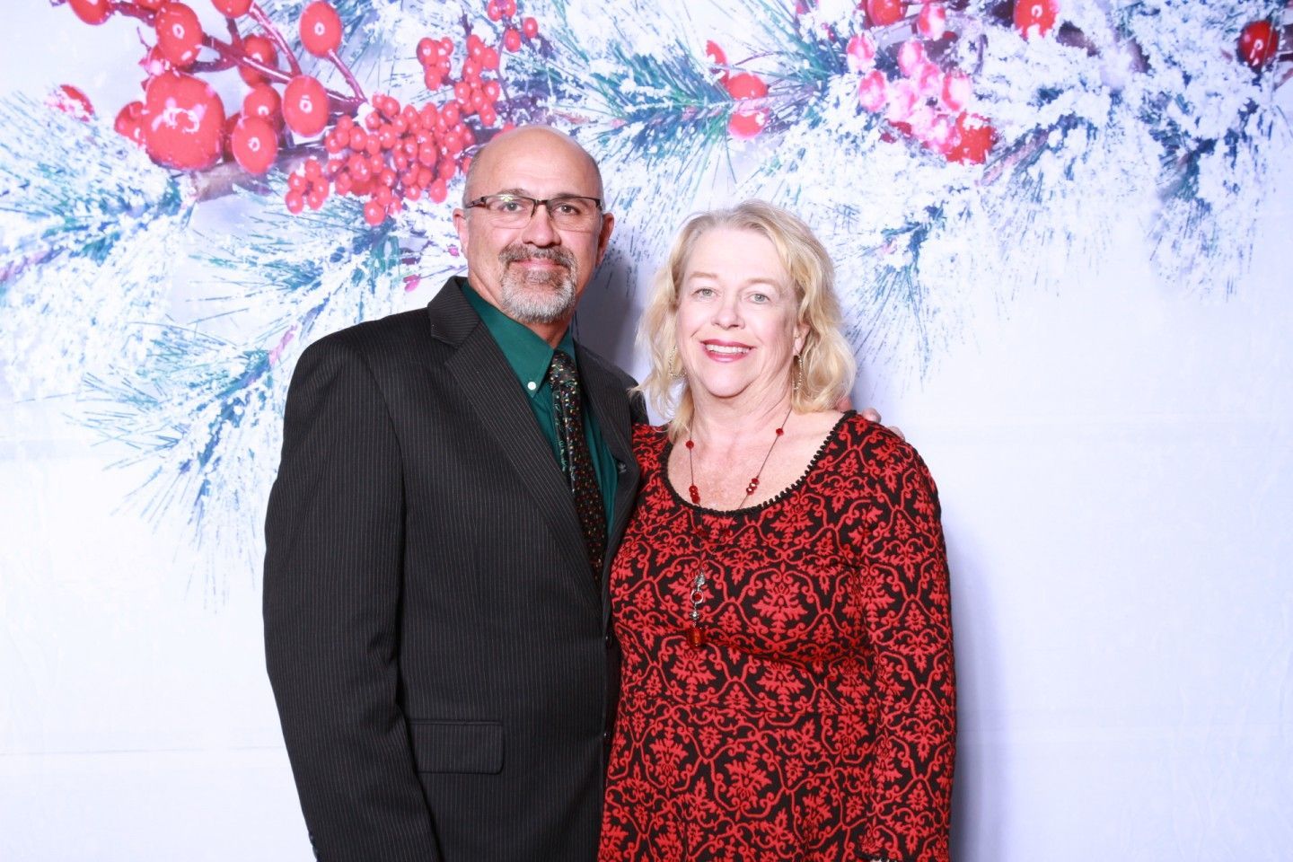 Couple posing in front of a holiday backdrop. The man wears a suit, and the woman wears a red dress.