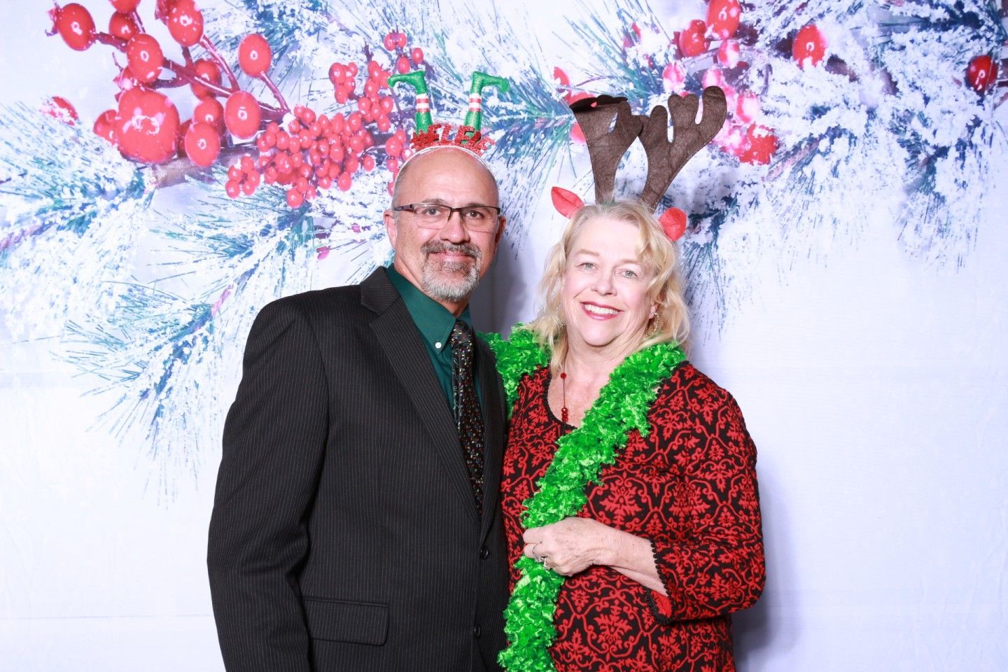 Couple posing for a photo, Christmas theme background; man in suit, woman wearing antlers and boa.