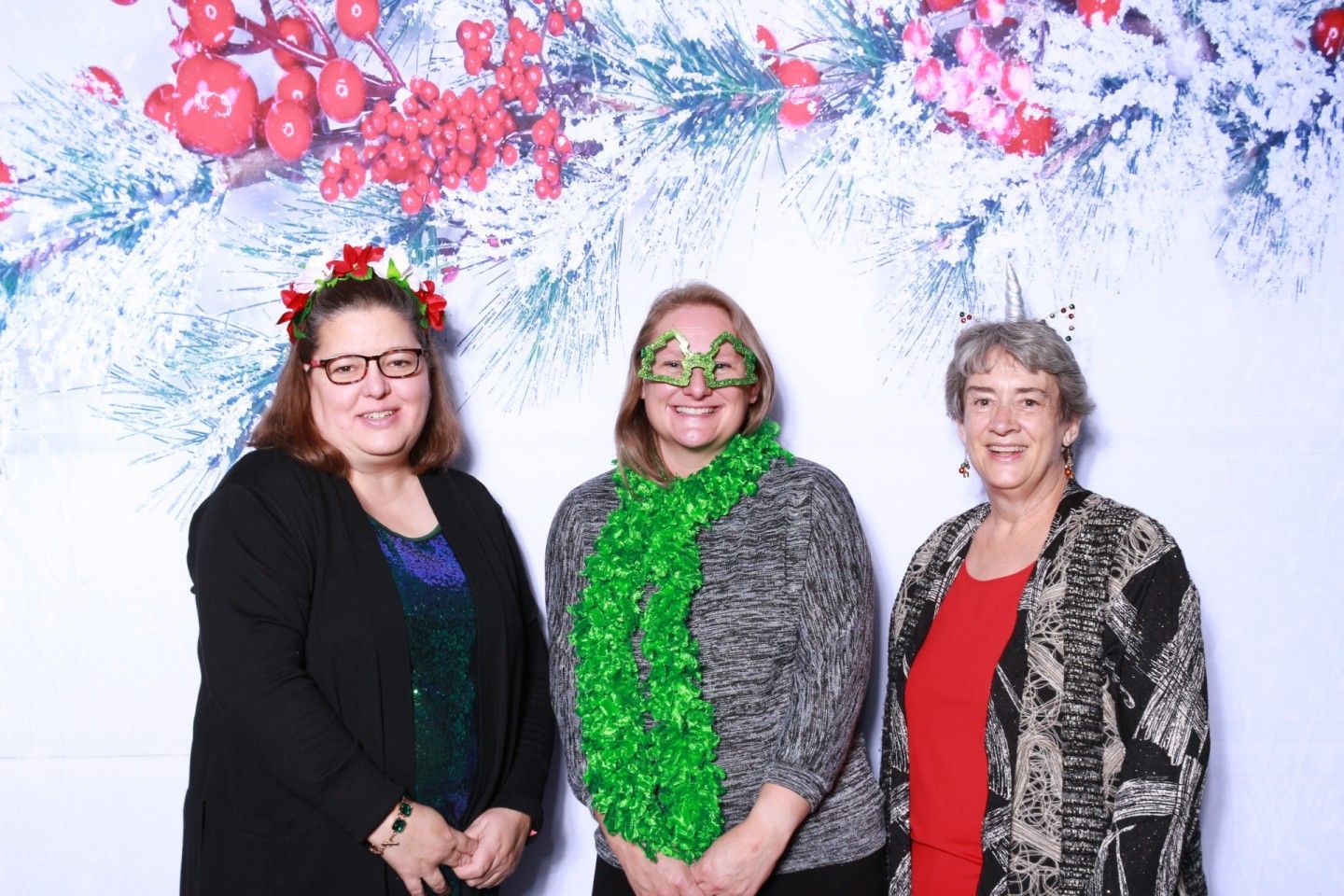 Three people smiling, posed in front of a holiday backdrop.