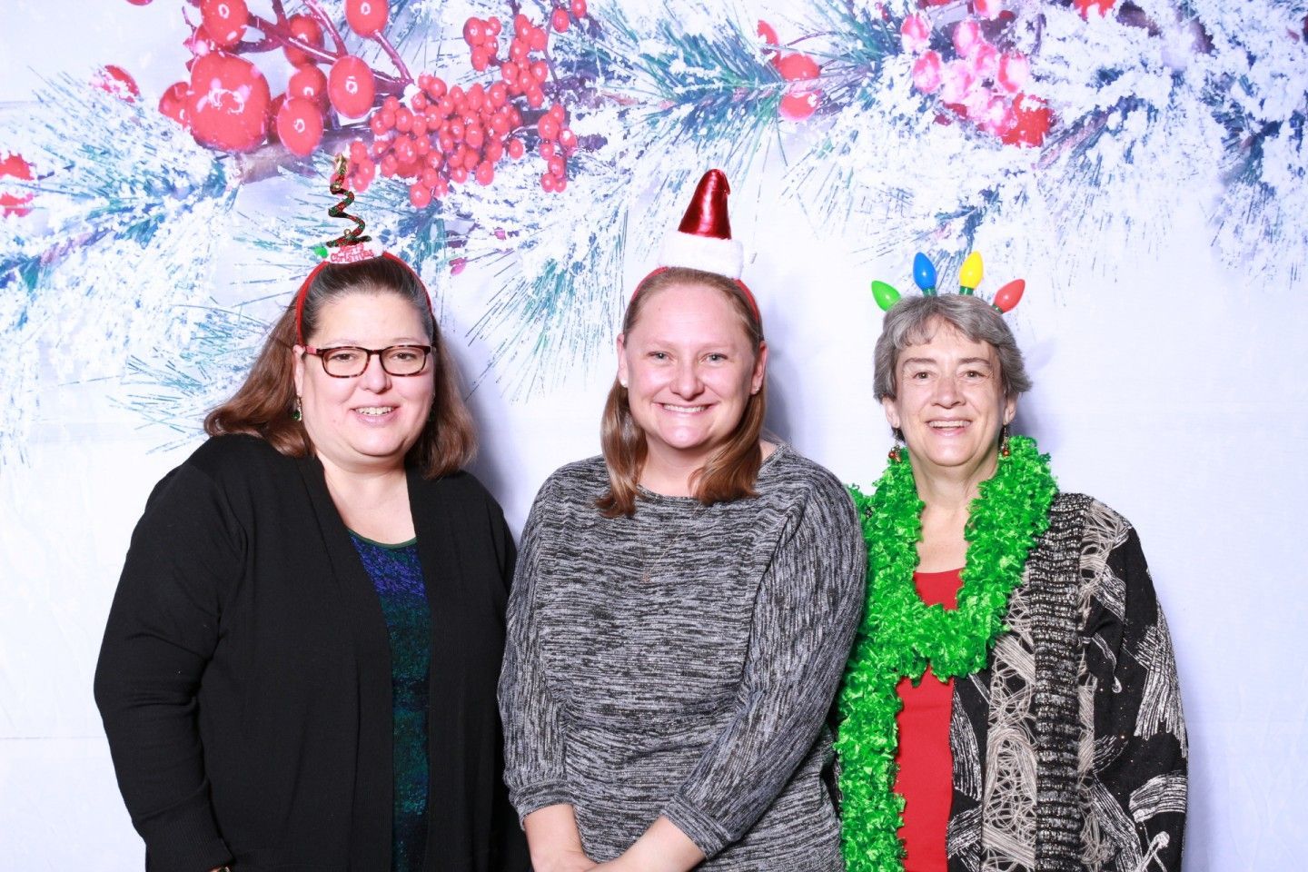 Three people wearing Christmas-themed headbands posing in front of a festive backdrop.