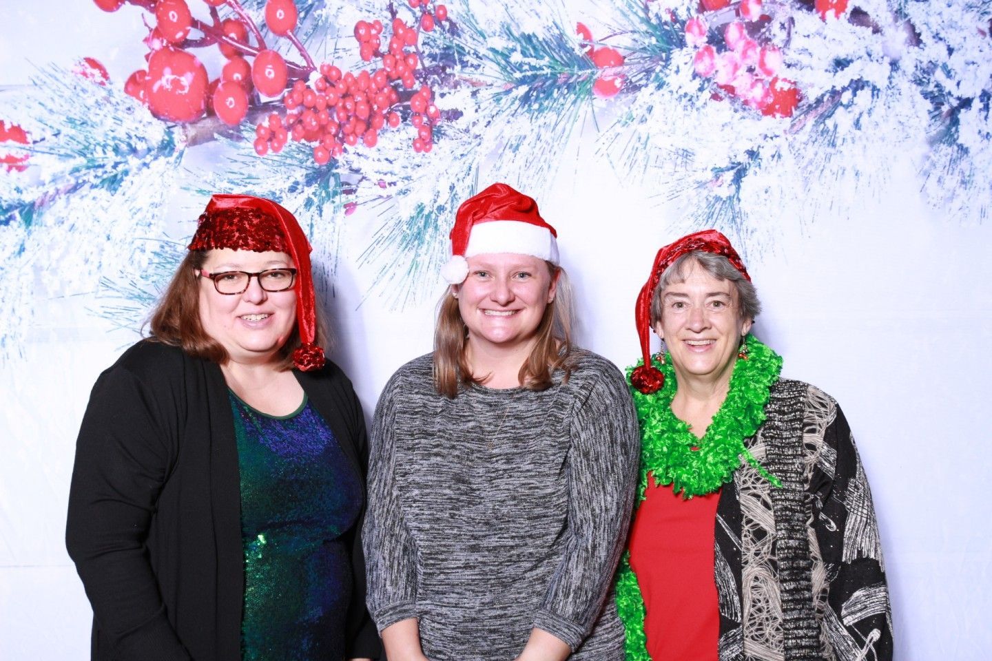 Three people in holiday attire posing in front of a festive backdrop.