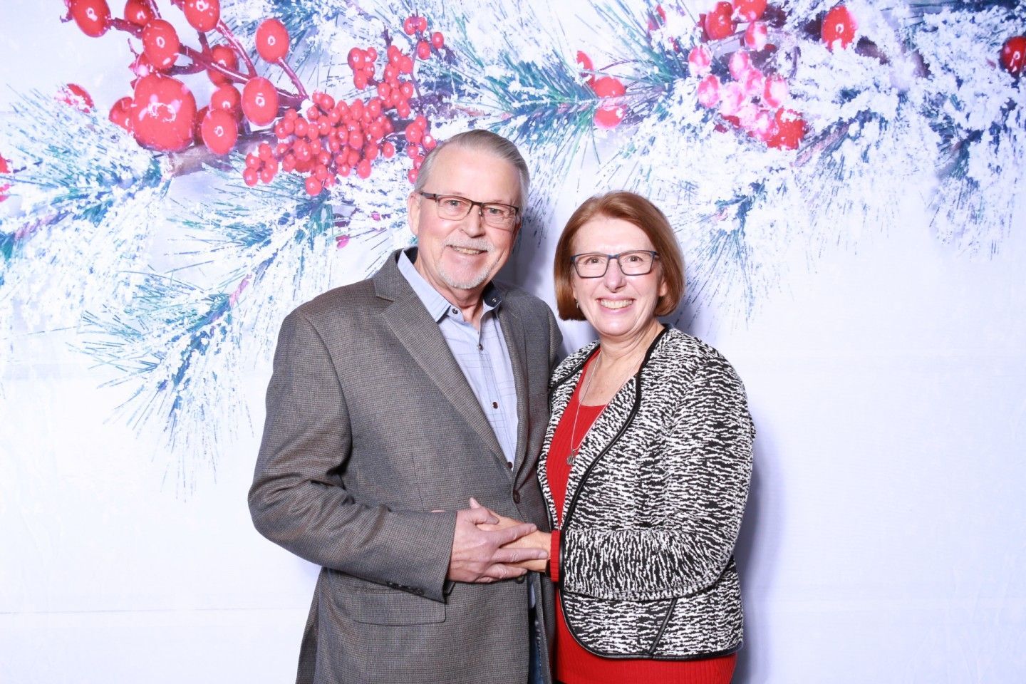 Older couple smiles, holds hands. Christmas background with red berries and snow.