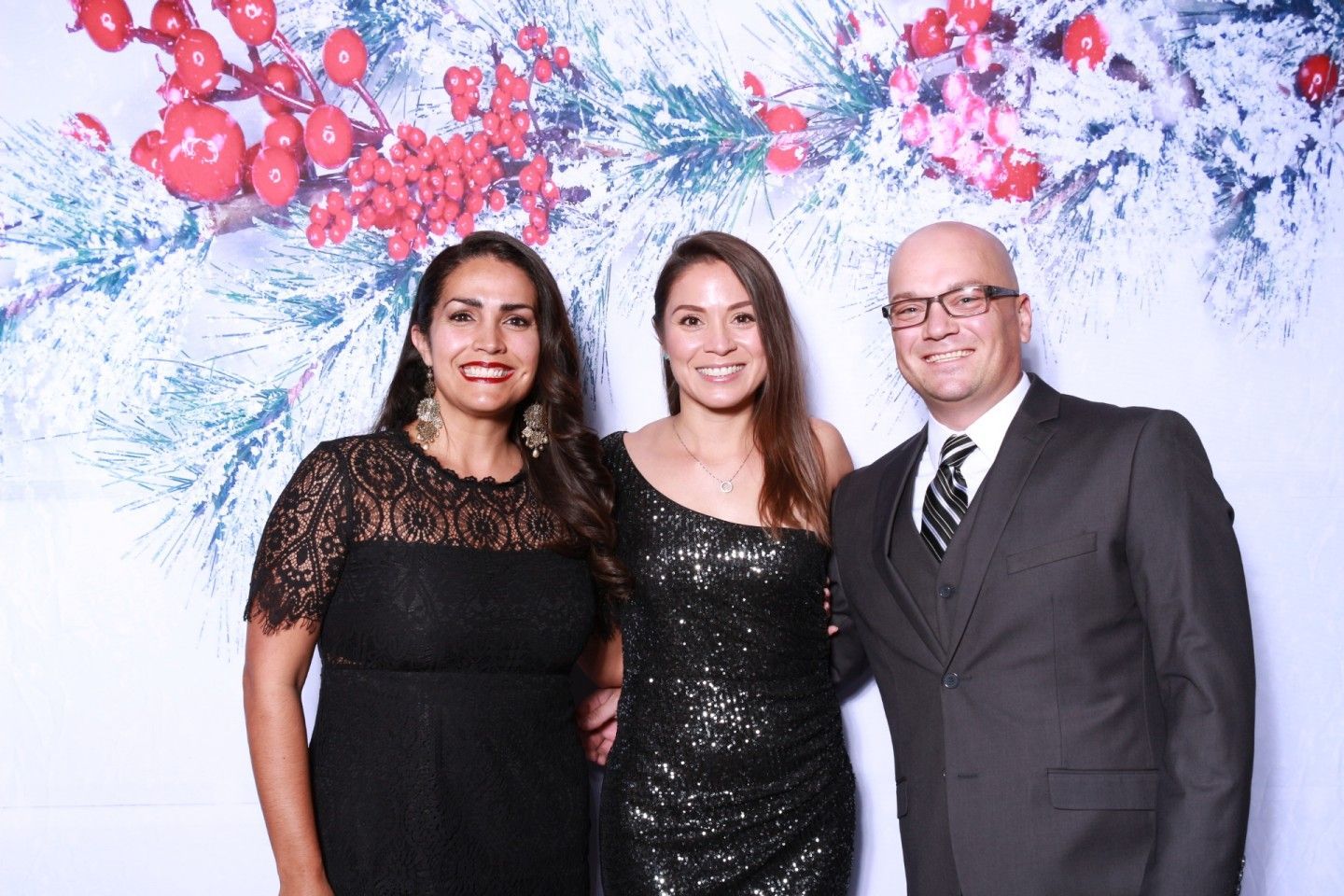 Three people posing in front of a holiday backdrop.