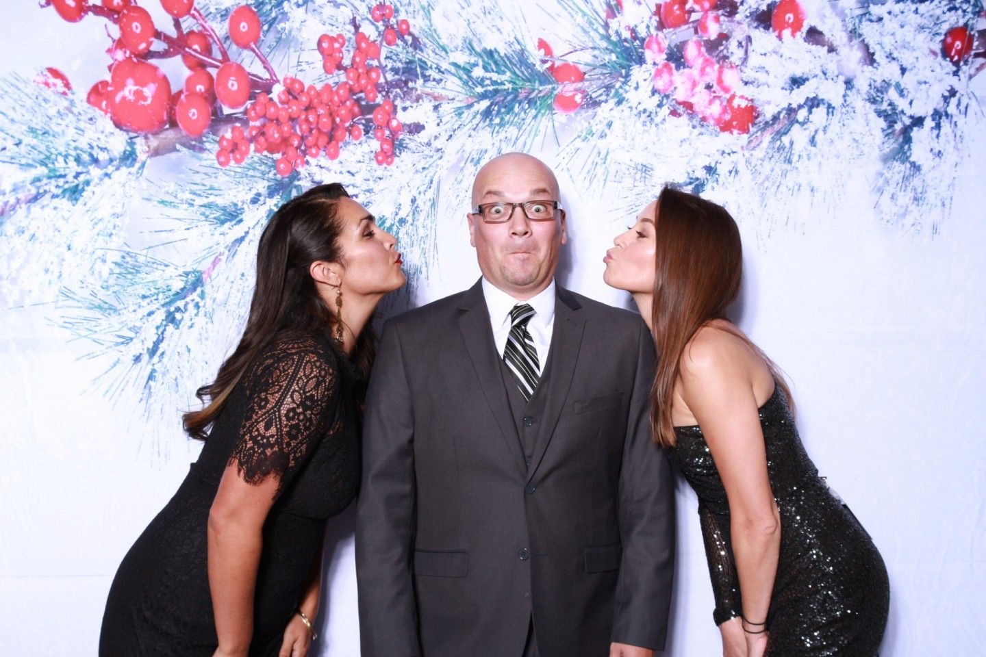 Man in suit flanked by two women blowing kisses. Festive backdrop with berries and snow.