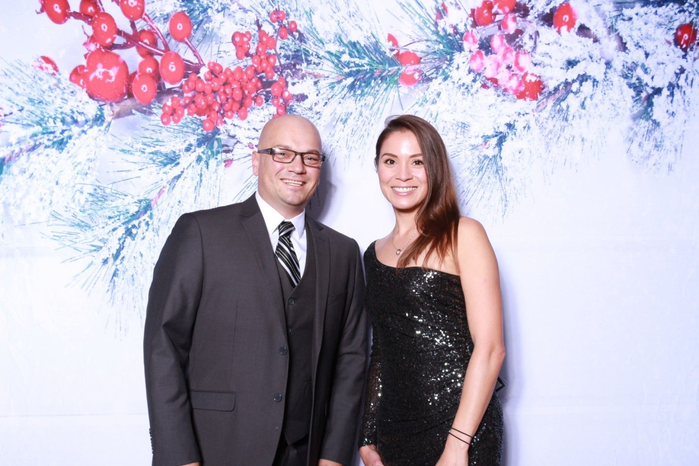 Man in suit and woman in sequined dress pose for photo, holiday backdrop.