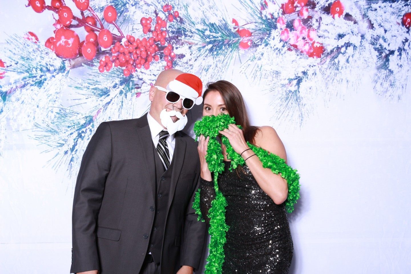 Man in suit and woman in sequined dress posing with Christmas photo booth props.