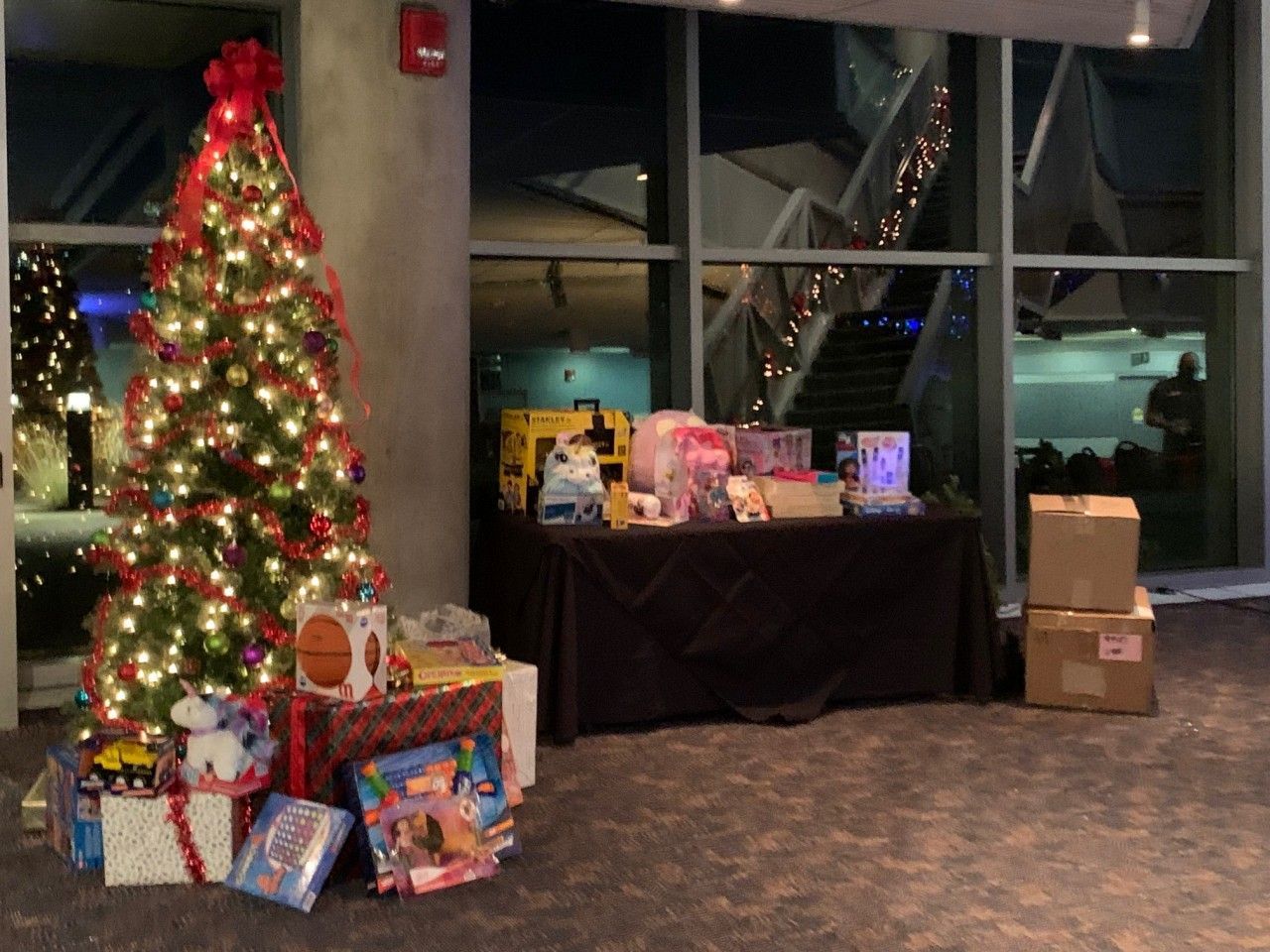 Christmas tree with presents next to a table of gifts in front of a window at night.