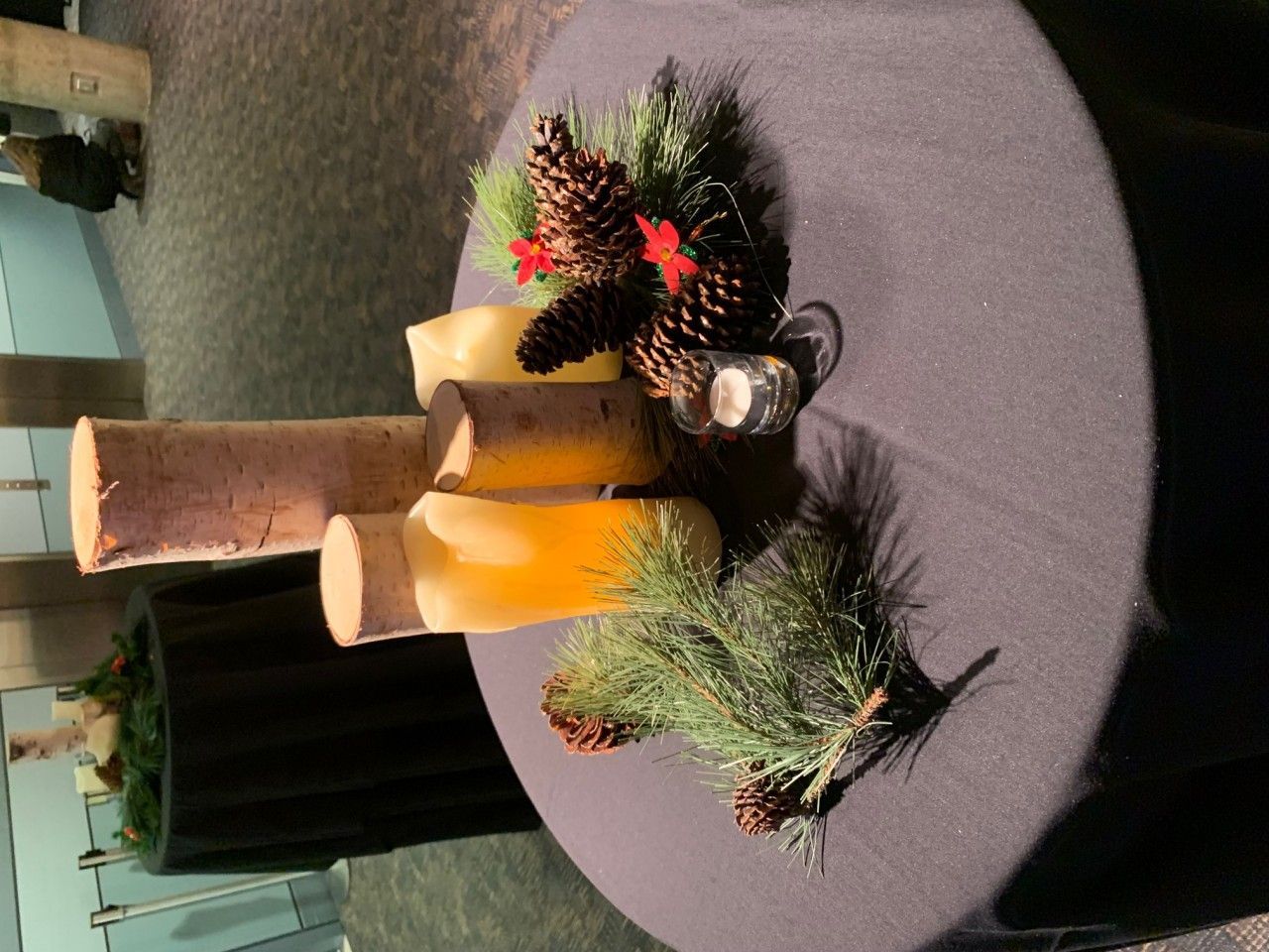 Centerpiece with pinecones, candles, and greenery on a black tablecloth.