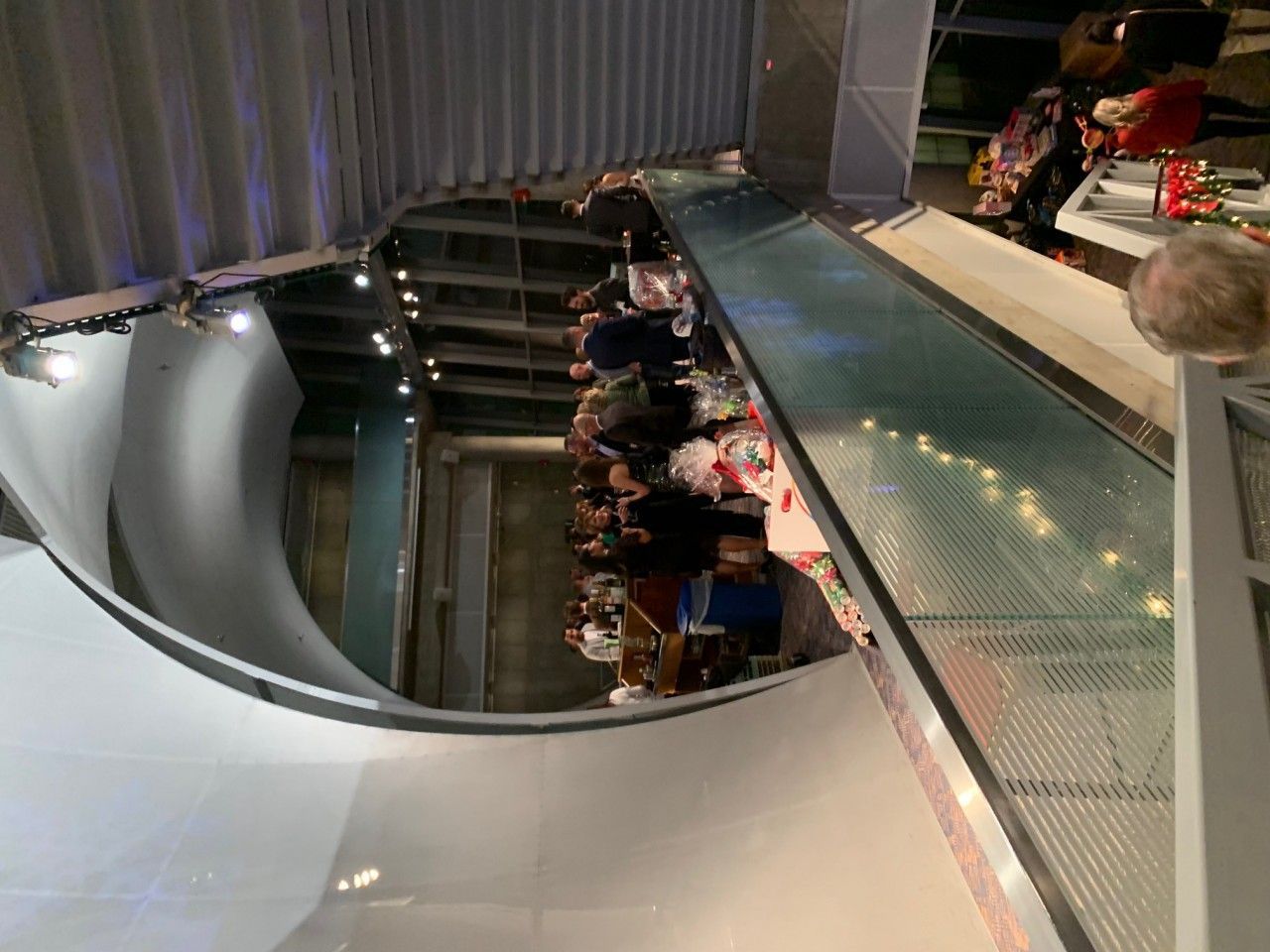 People on a long escalator ascending a building. The escalator is next to a curved wall.