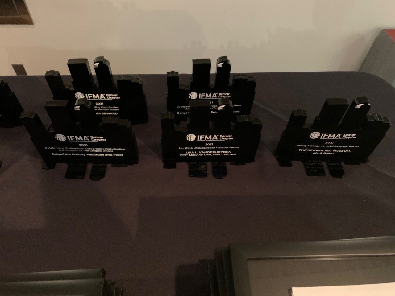 Six black awards on a table. Each has a logo and text.