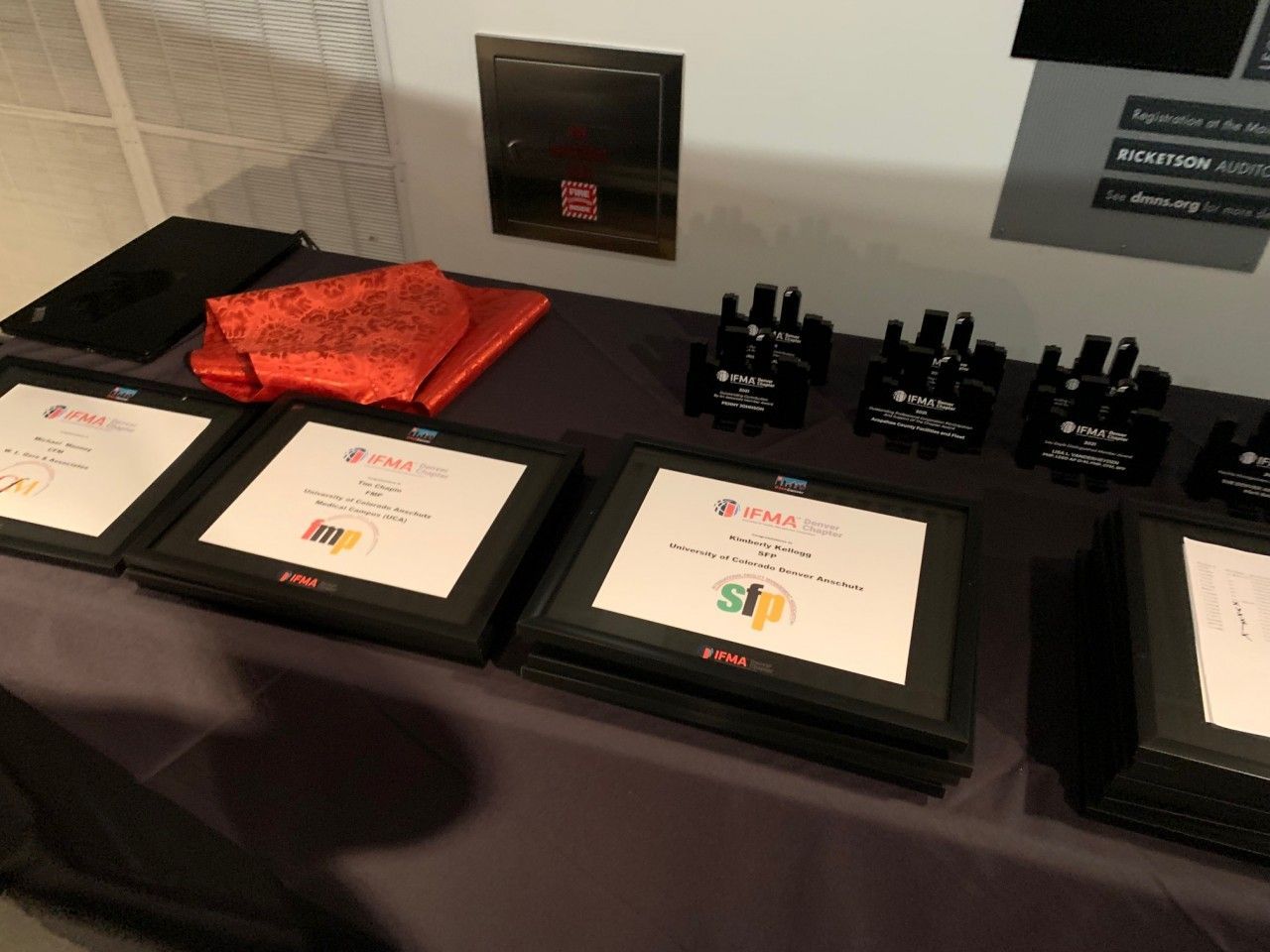 Awards and black swag on a table, with a red cloth. A box is mounted on the wall.