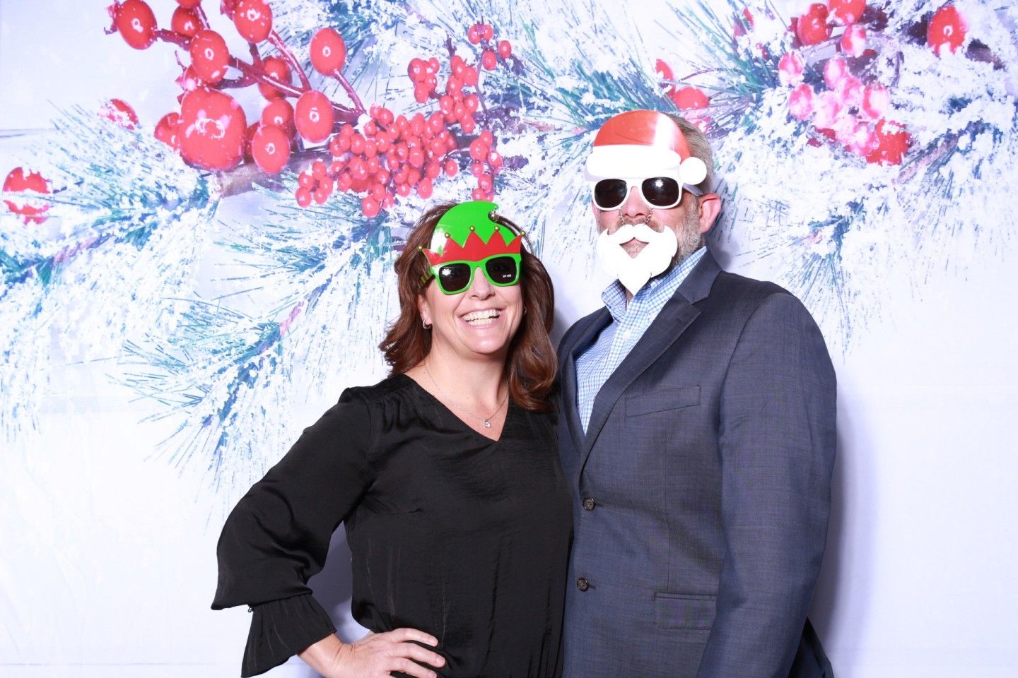 Woman and man posing for photo, wearing novelty Christmas glasses and in front of a festive backdrop.