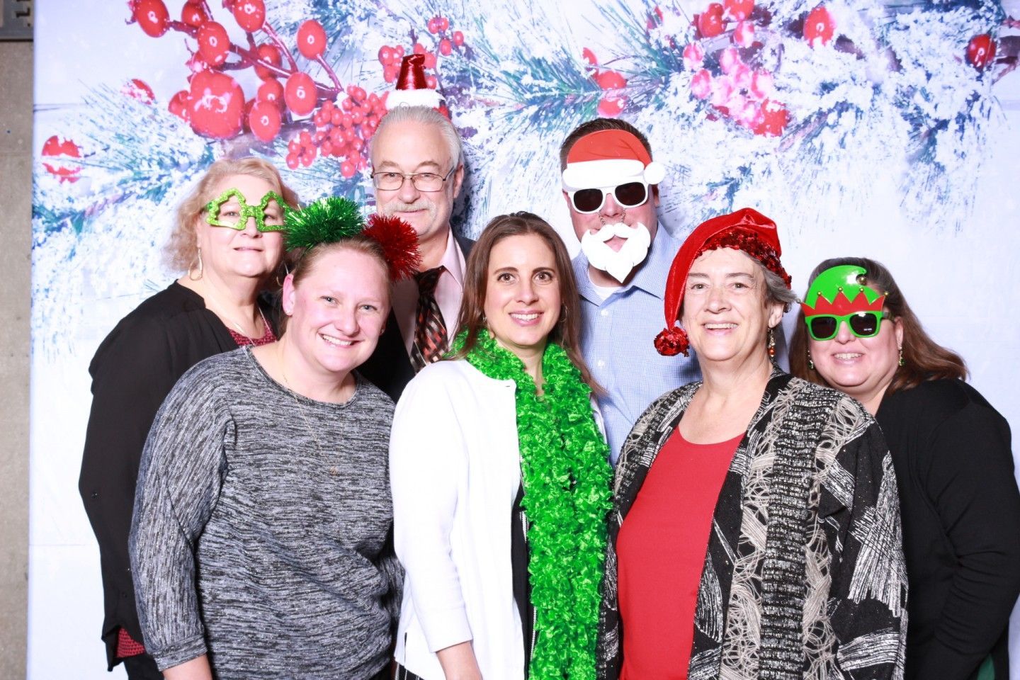Group of people wearing festive holiday props pose in front of a Christmas-themed backdrop.