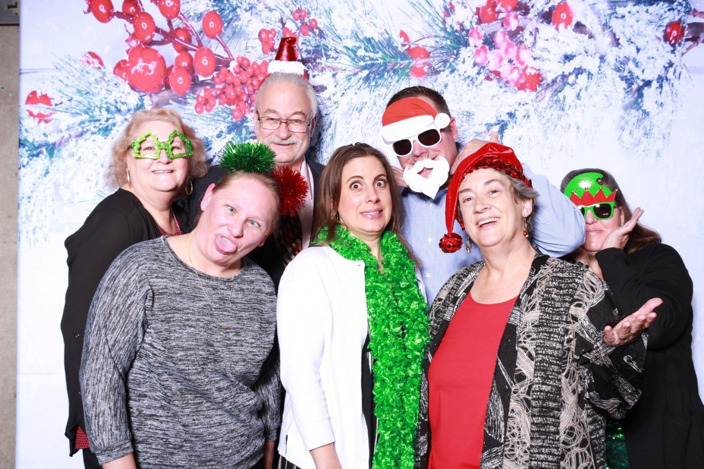 Group of people posing with holiday props, making silly faces in front of a festive backdrop.