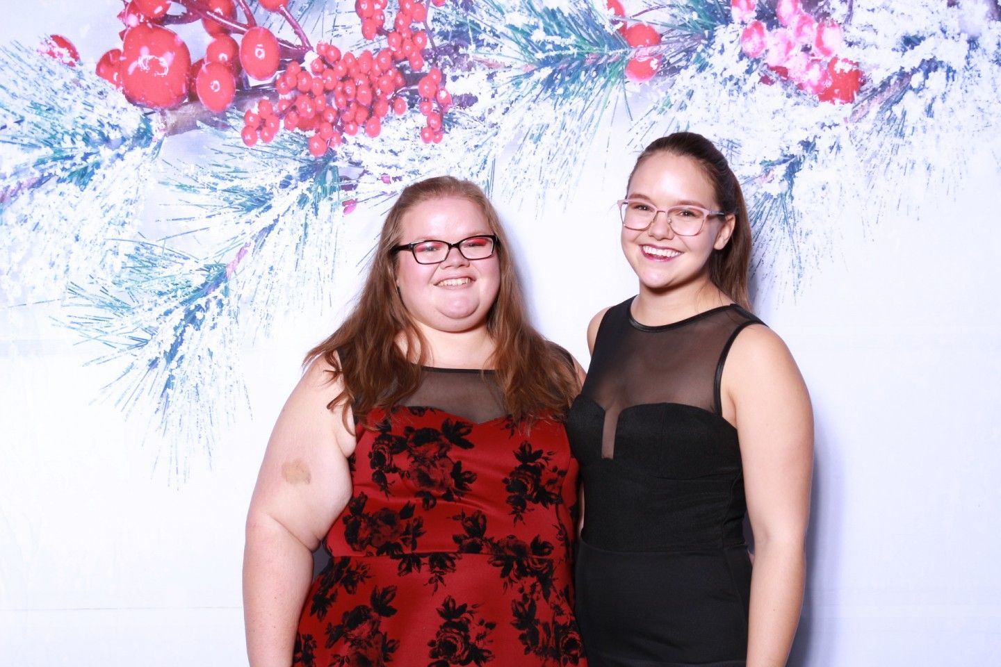 Two women in formal dresses pose in front of a winter-themed backdrop, smiling.