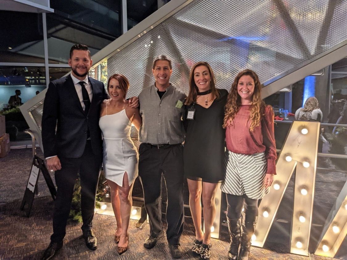 Five people pose together outdoors in front of lit-up