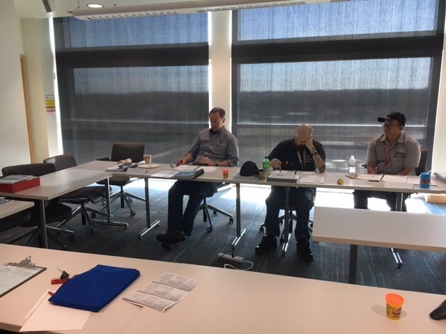 Three people seated at a table in a meeting room with large windows.