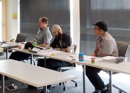 Three people seated at a table, working on papers in a well-lit room.
