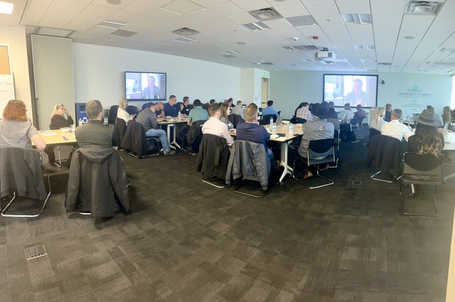 People seated at tables in a conference room, facing screens.