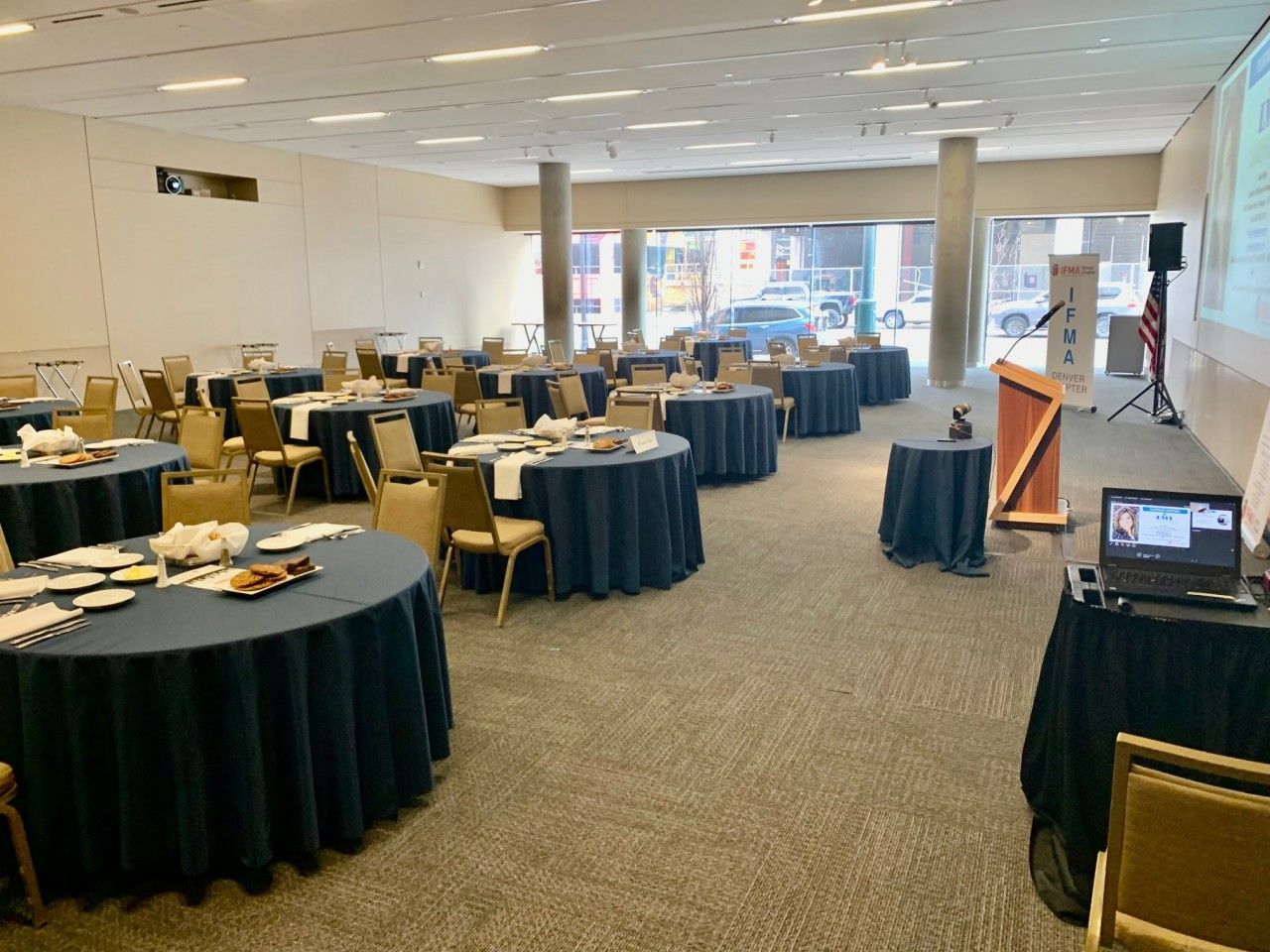 Empty conference room with round tables covered in blue tablecloths, chairs, and a podium.