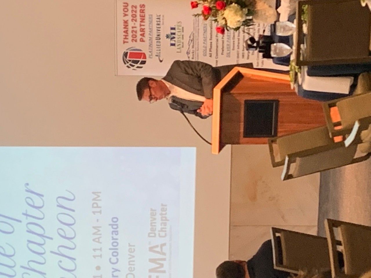 Man speaking at a podium in Denver, Colorado. Sign reads 