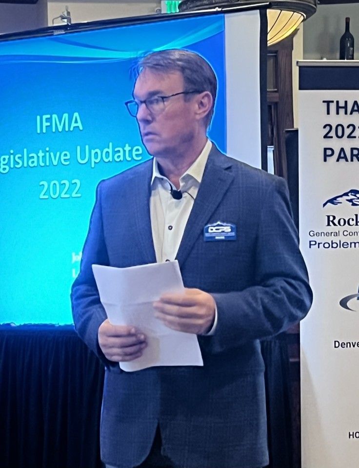 Man in suit holds paper, speaks at IFMA Legislative Update 2022 presentation.