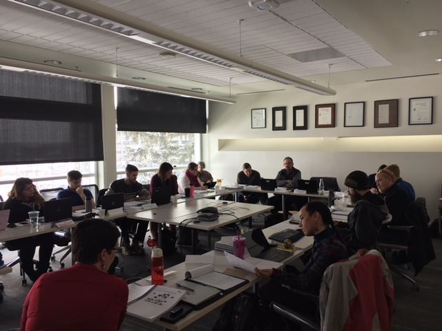 People at a table in a bright meeting room, discussing documents. Window with snow outside.