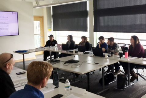 People seated at a table in a meeting room with laptops, looking at a screen displaying text.