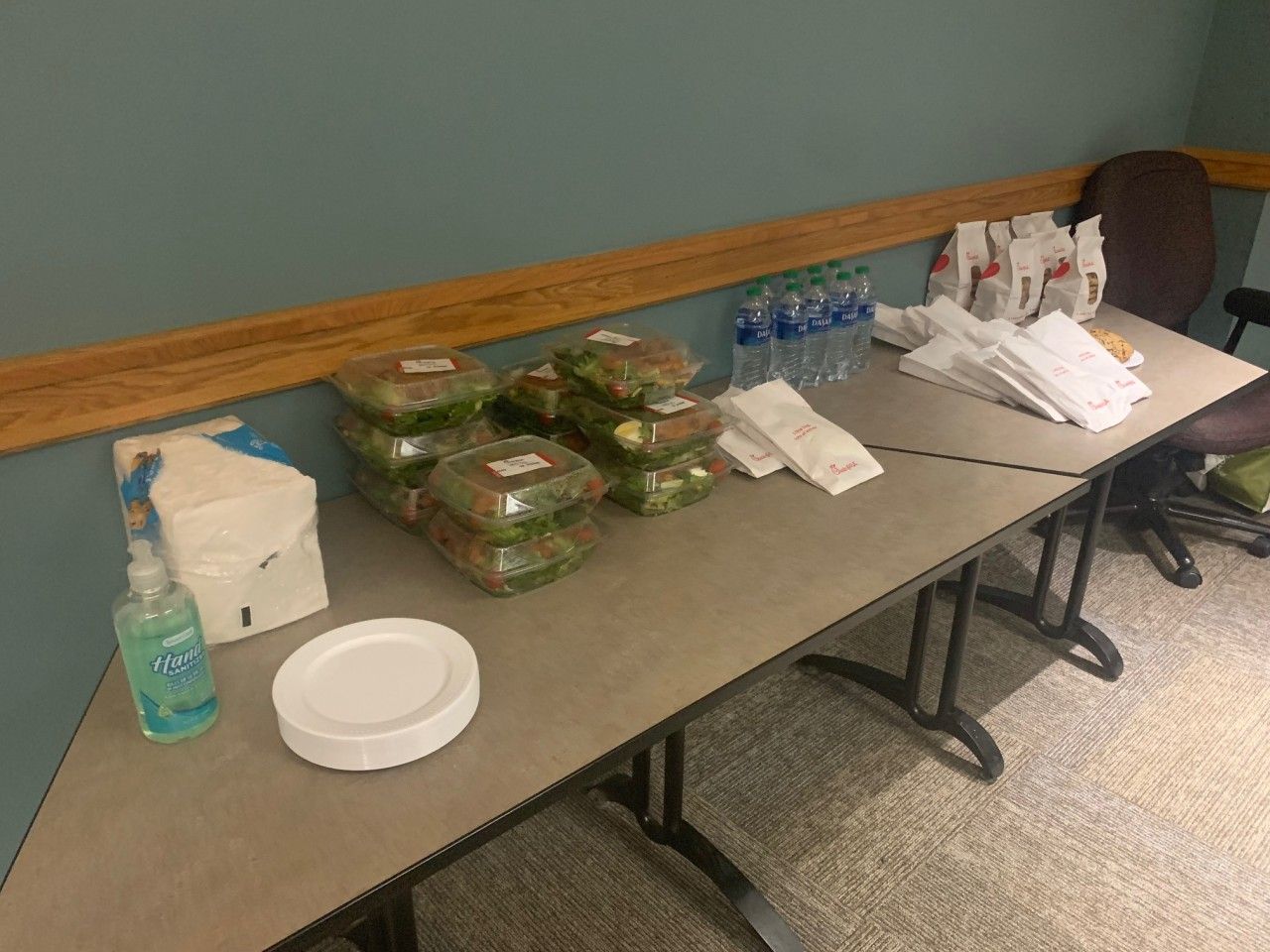 Table with pre-packaged meals, water bottles, and hand sanitizer. Paper plates and napkins are also present.
