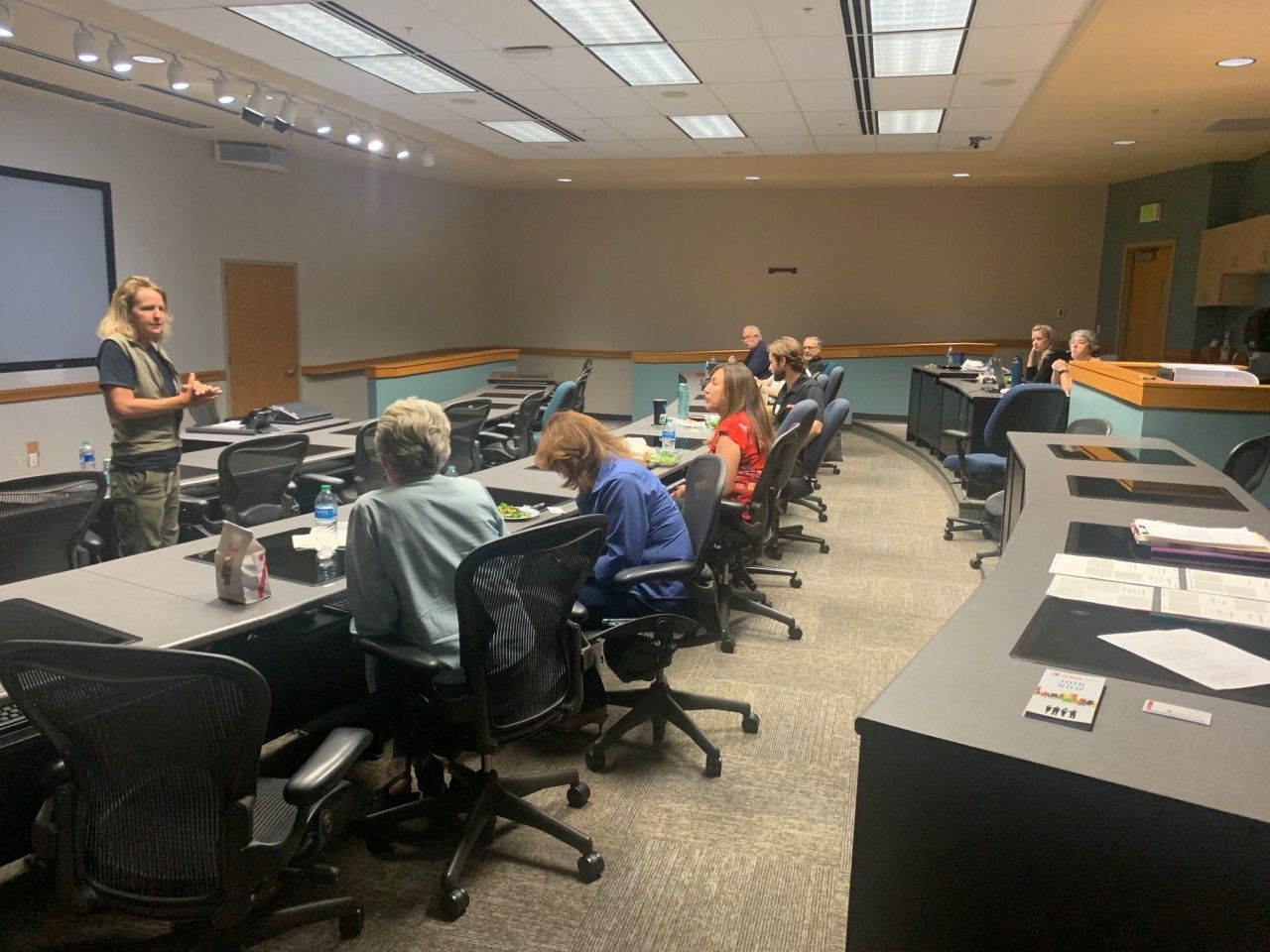 Man presenting in a conference room with a group seated at long tables.