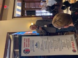 Man speaking at a conference, with a banner thanking sponsors.