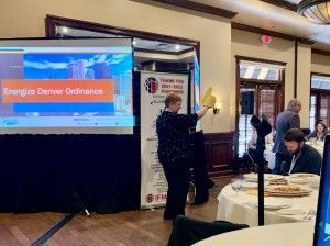 A woman presents at a conference, holding a yellow object