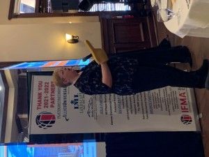 Woman giving a presentation, pointing up with a glove. A banner saying 