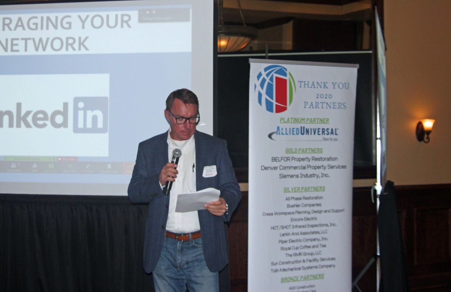 Man speaking at podium, presentation about LinkedIn on screen, banner with partner logos.