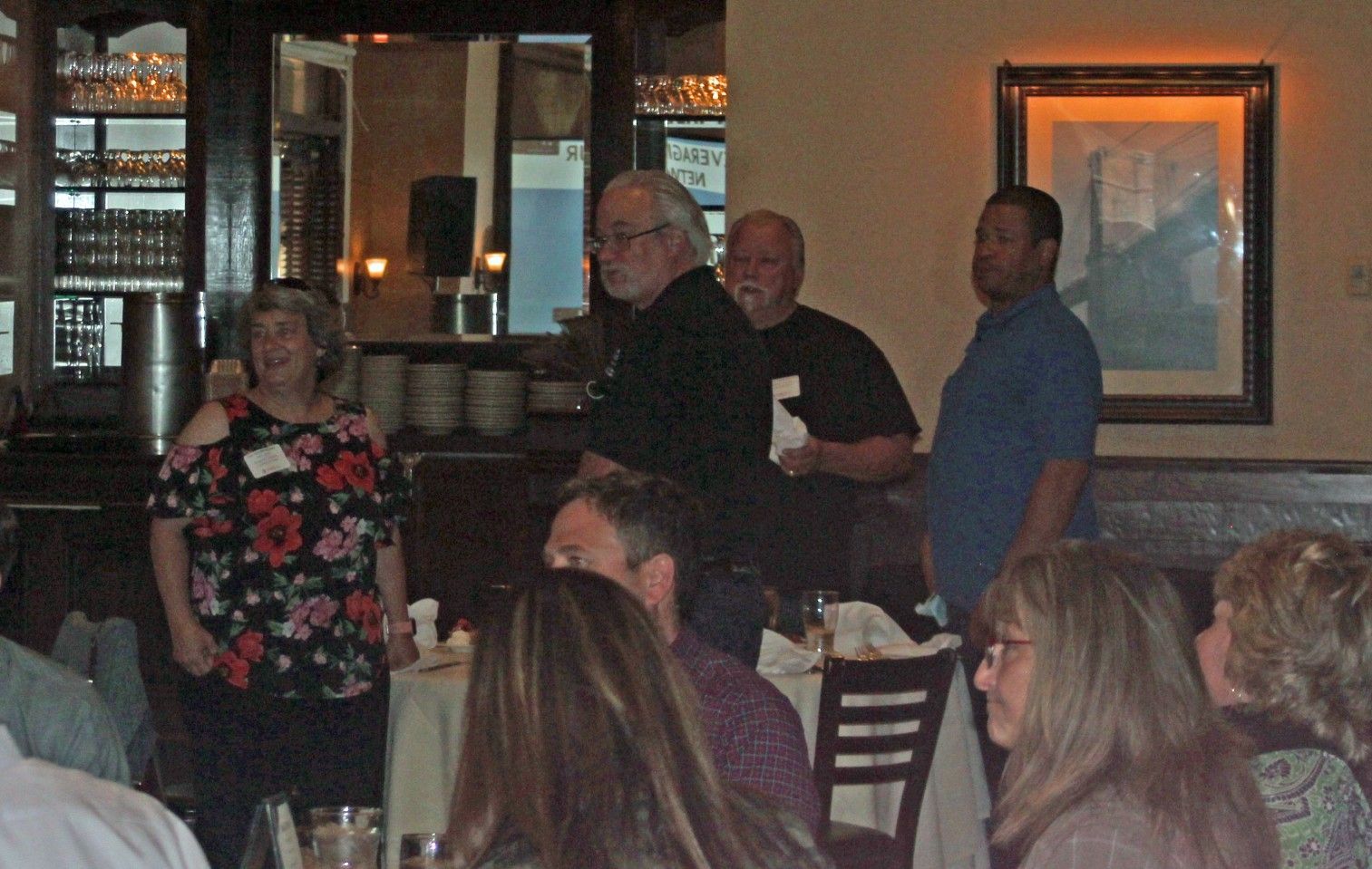 People at a restaurant, one woman speaks. Others stand near tables. Dark wood interior.