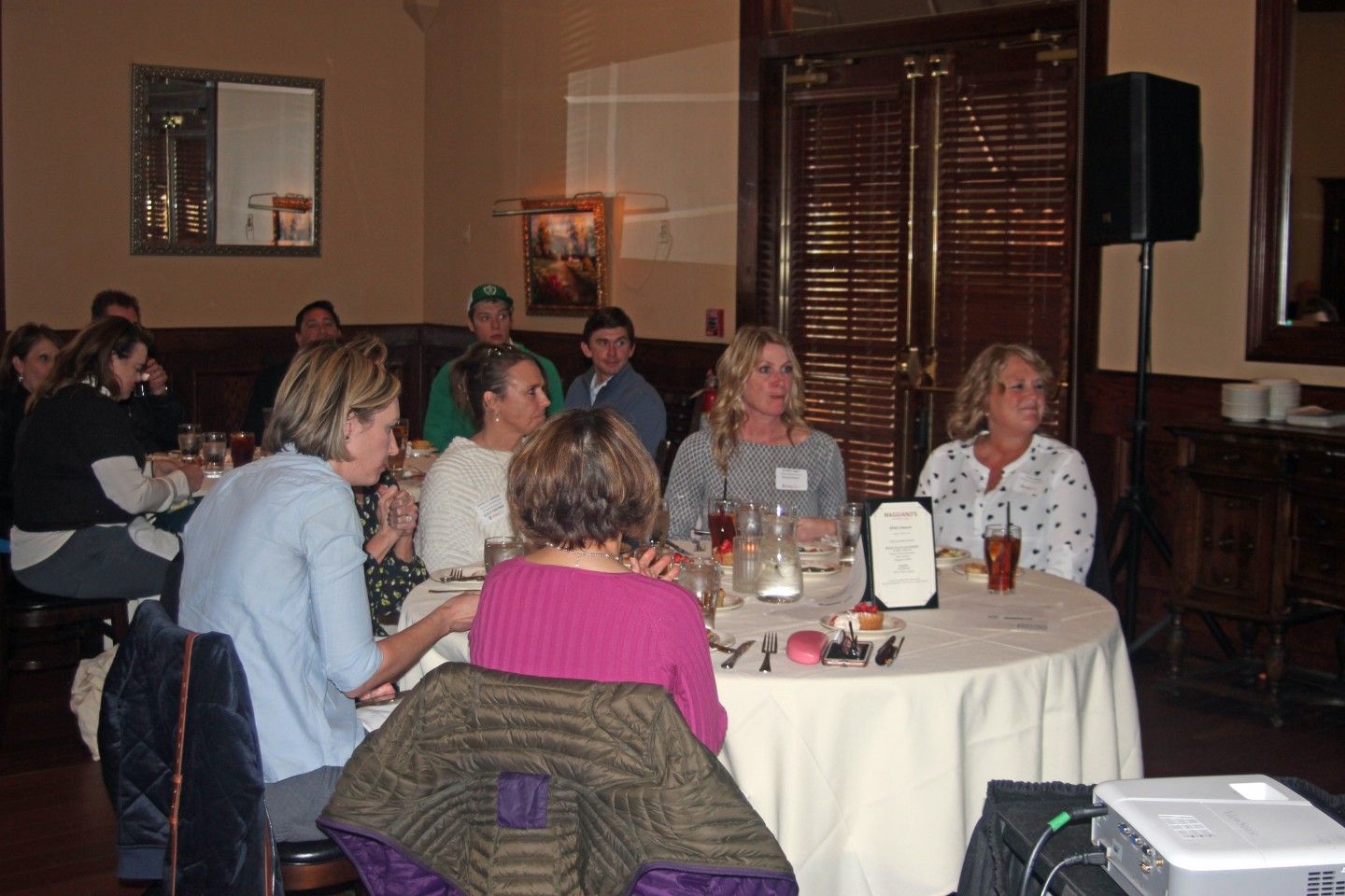 People seated at a round table, possibly a panel, in a restaurant. Others are seated at tables in the background.