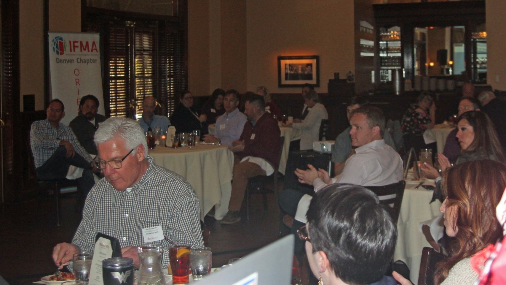 People at round tables in a restaurant for a meeting; IFMA banner visible.