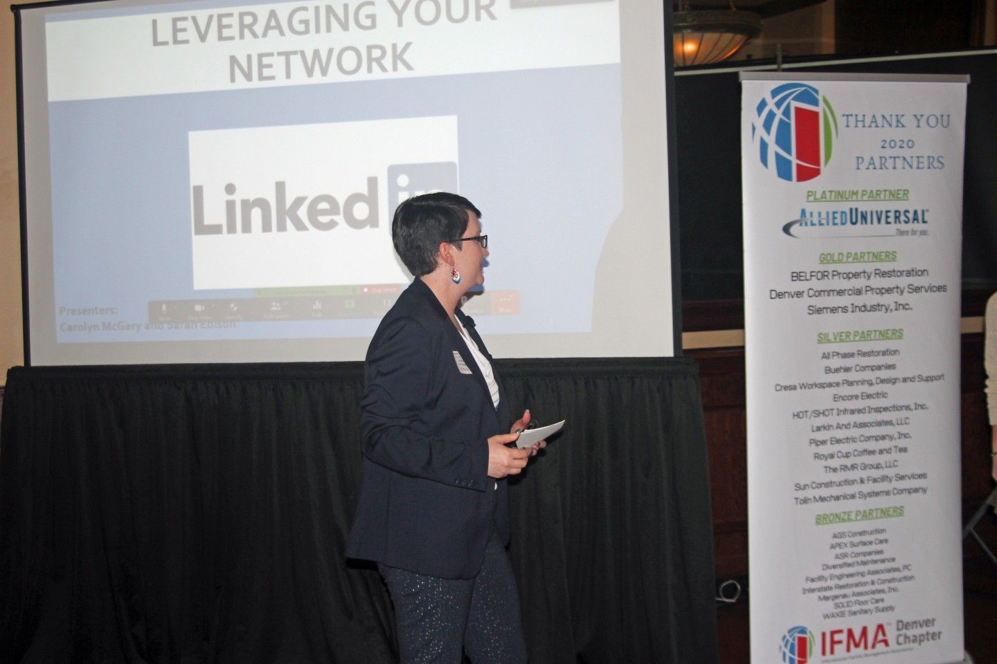 Woman giving a presentation on LinkedIn, standing next to a screen and a banner that says