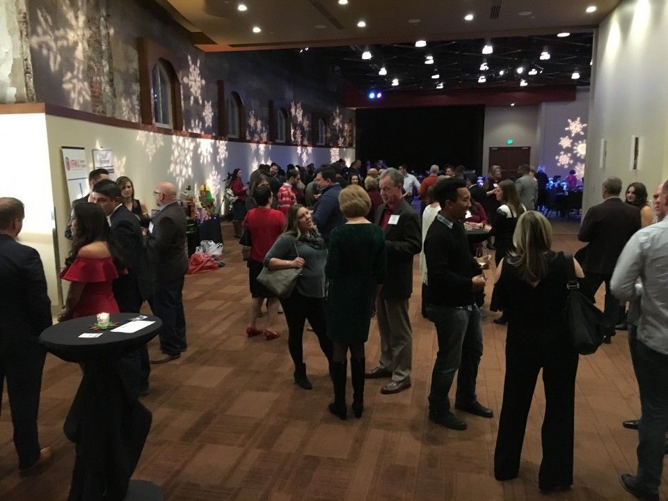Event in a large room with people, some wearing business attire, conversing. Snowflake decorations on walls.