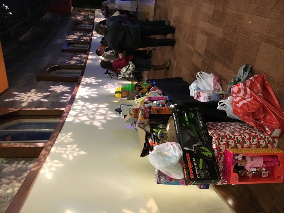 People and toys line a long table with snowflake decorations, presumably for a holiday event.