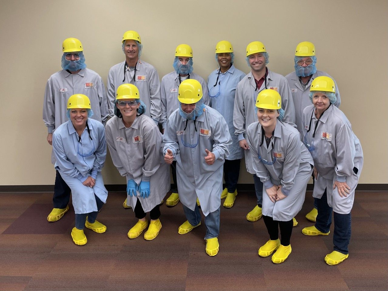 Group of people in protective gear, yellow hard hats, and shoes, posing in a room.