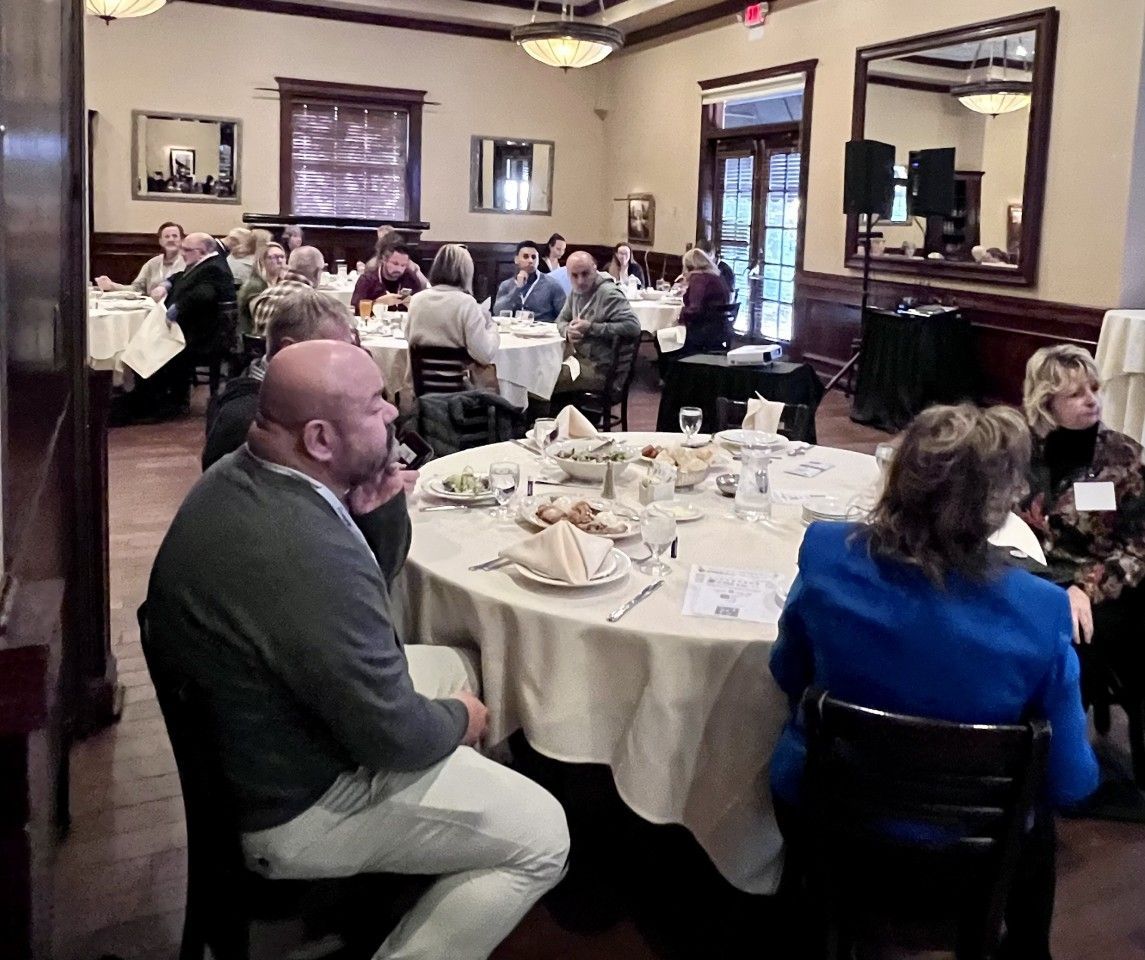 Group of people seated at round tables in a restaurant, appearing to attend a meeting.